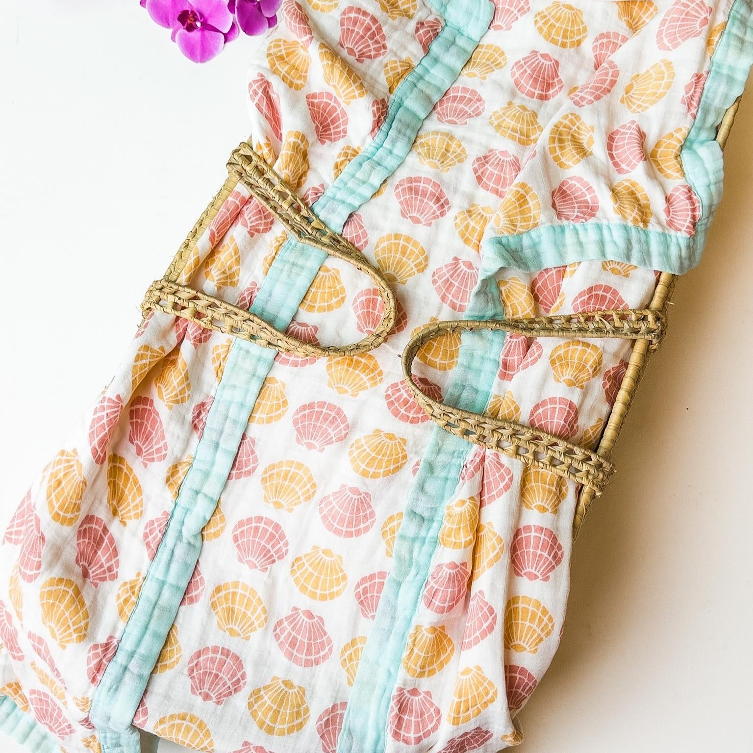 organic seashell print luxe baby blanket. Beige, soft pinks, oranges with coral trim.
