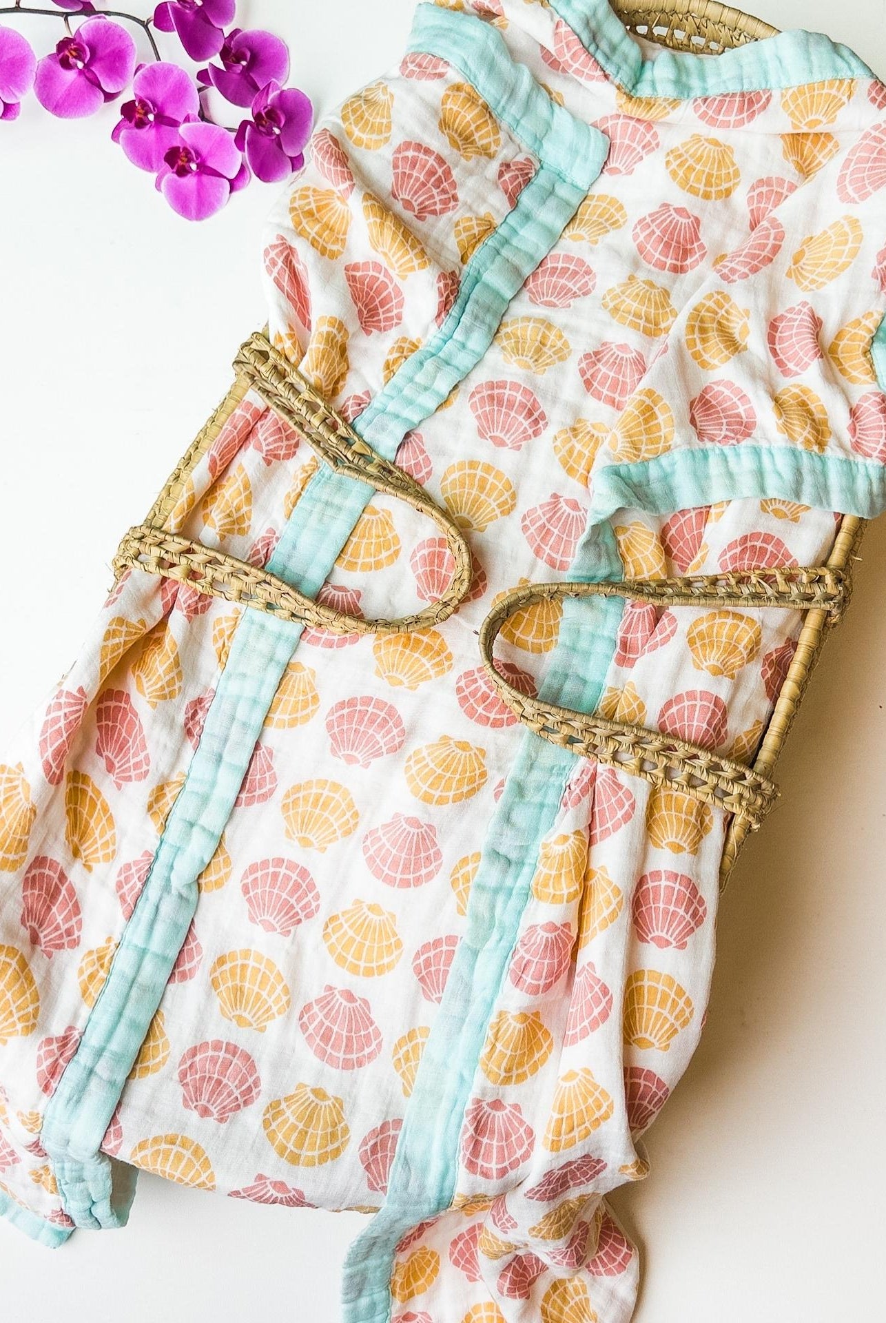 organic seashell print luxe baby blanket. Beige, soft pinks, oranges with coral trim.