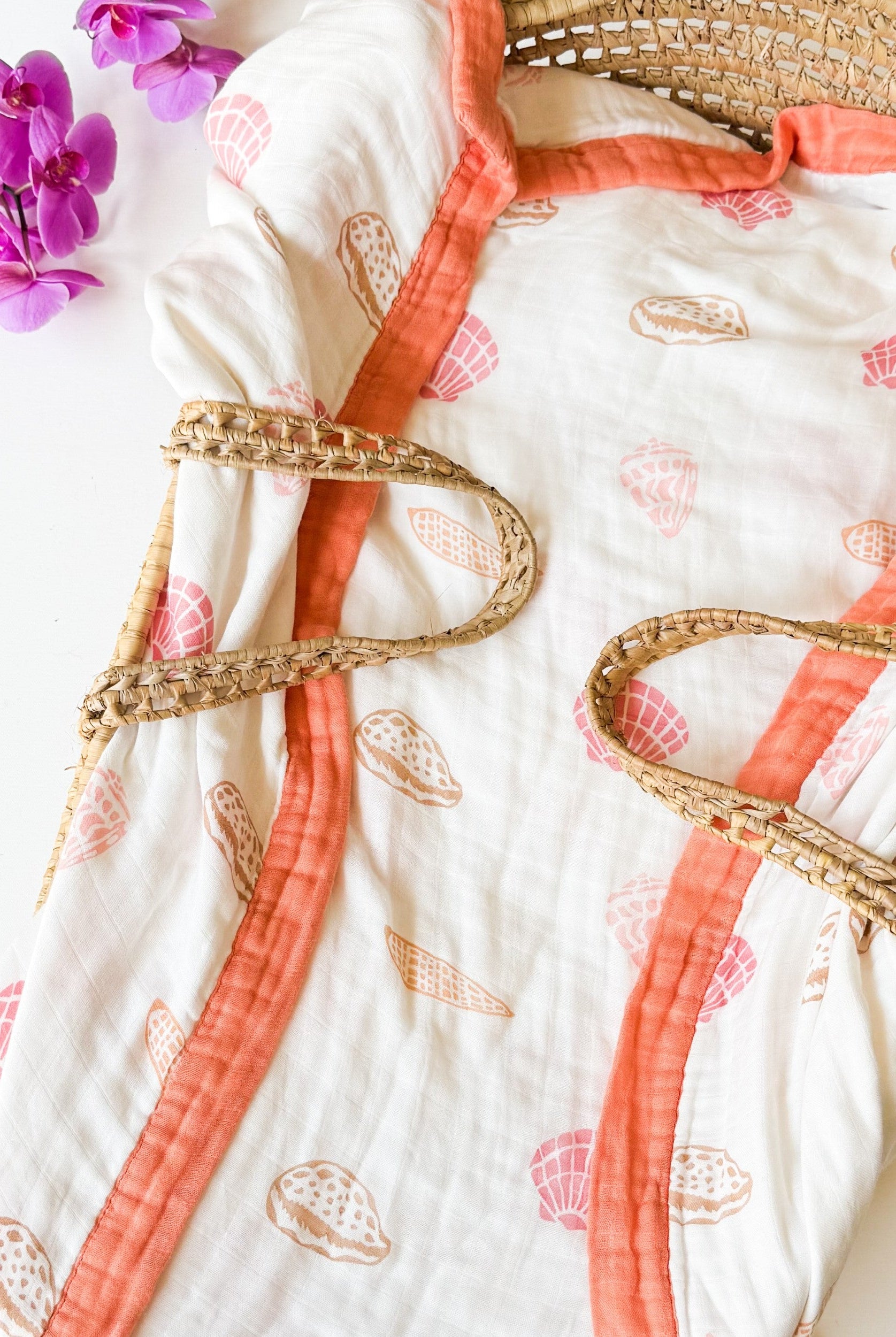organic seashell print luxe baby blanket. Beige, soft pinks, oranges with coral trim.