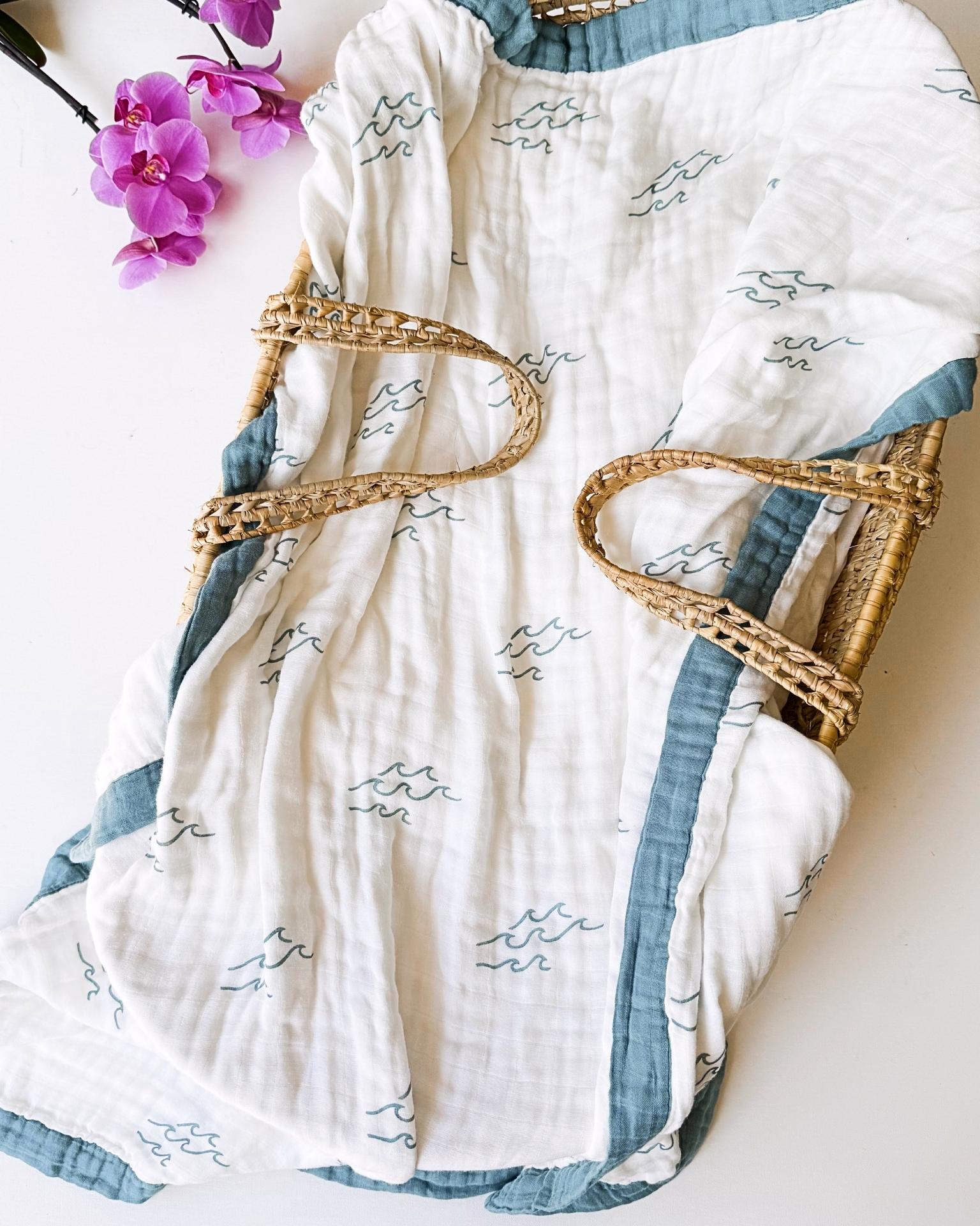 White and blue wave patterned blanket draped over a wicker basket with purple flowers in the background