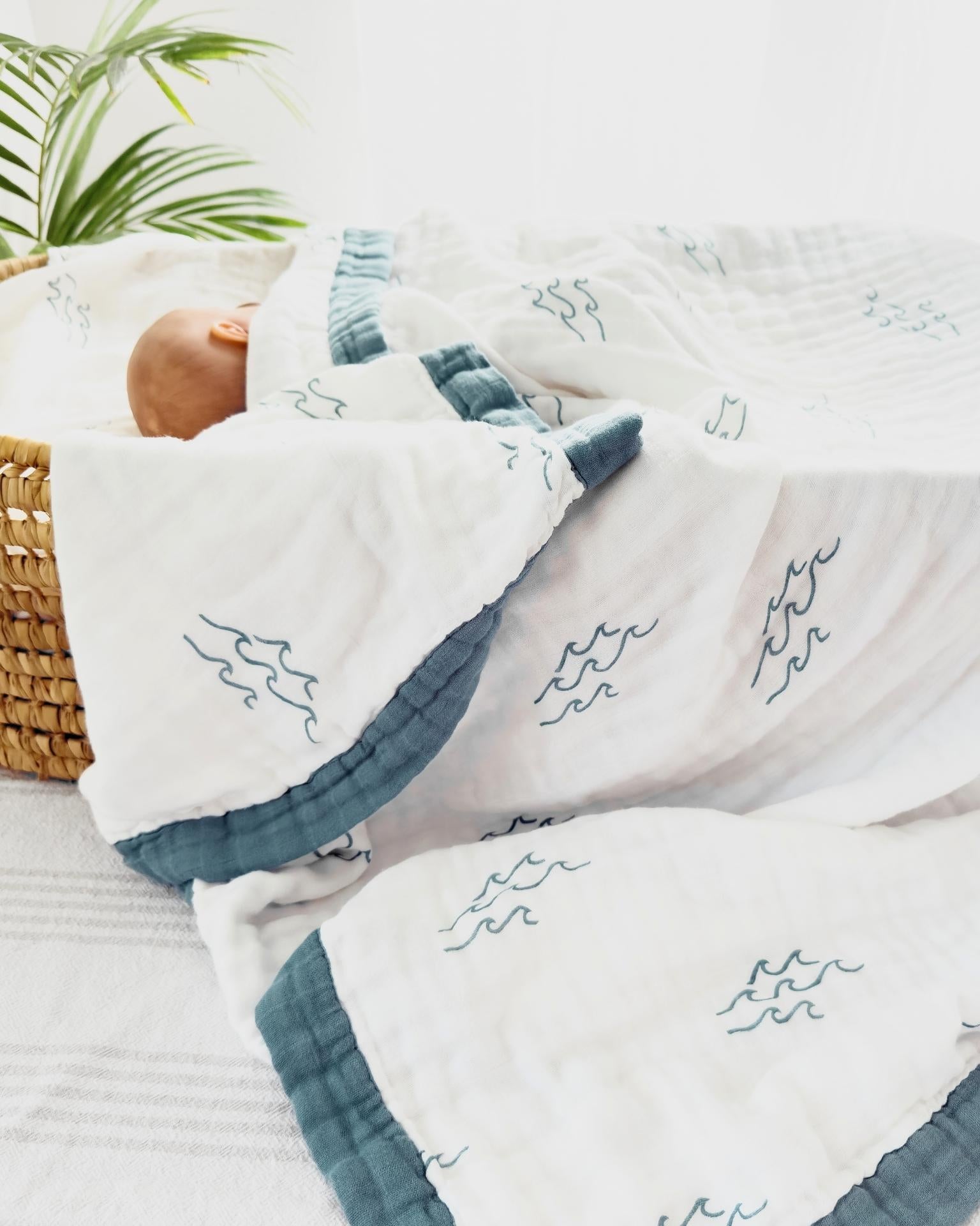 Baby wrapped in a white blanket with blue wave patterns, lying on a white surface.