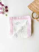Baby blanket with pink border and wave design on a white surface with flowers and a basket